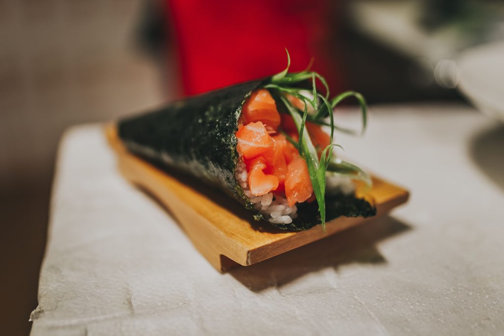 Delicious temaki sushi cone with salmon and seaweed on a wooden plate, highlighting Japanese cuisine.