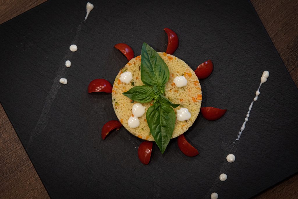 Couscous dish creatively plated with basil and cherry tomatoes on a slate plate.