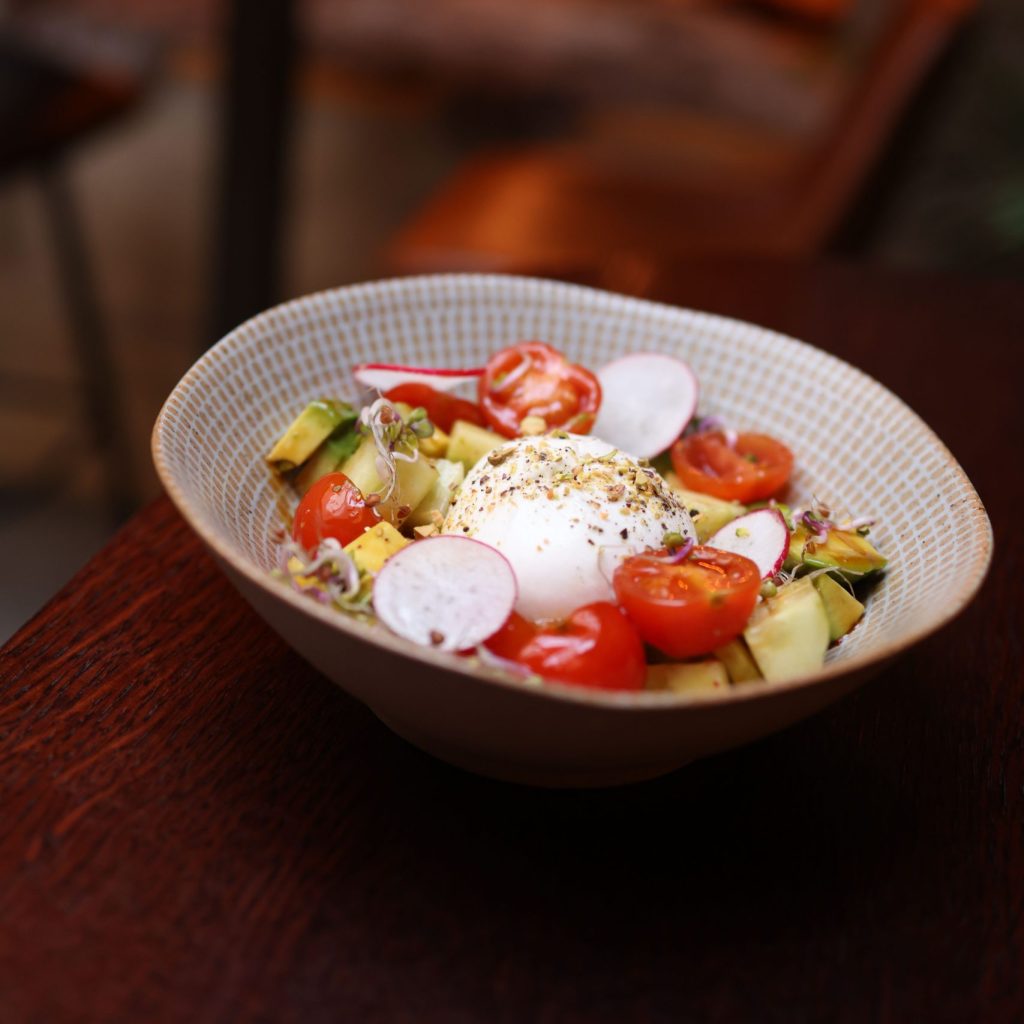 A fresh salad with avocado, tomatoes, radishes, and poached egg in a warm, inviting setting.
