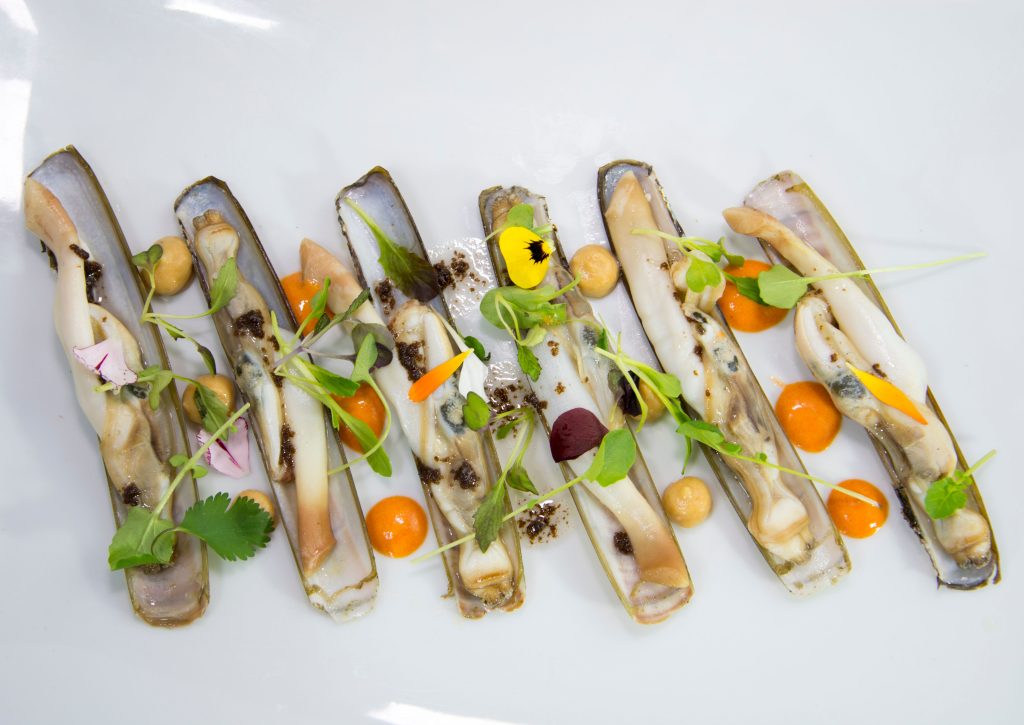 Elegant presentation of razor clams garnished with edible flowers and microgreens, offering a vibrant culinary experience.